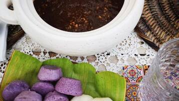 A table with a white ceramic pot containing a dark soup, a bowl of purple and white round food items, and a clear glass.
