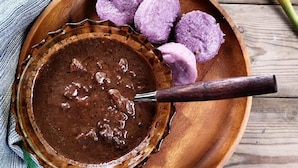 A bowl of chocolate spread with a spoon, accompanied by purple round items on a wooden plate. - Balai Vittorio (Oton)