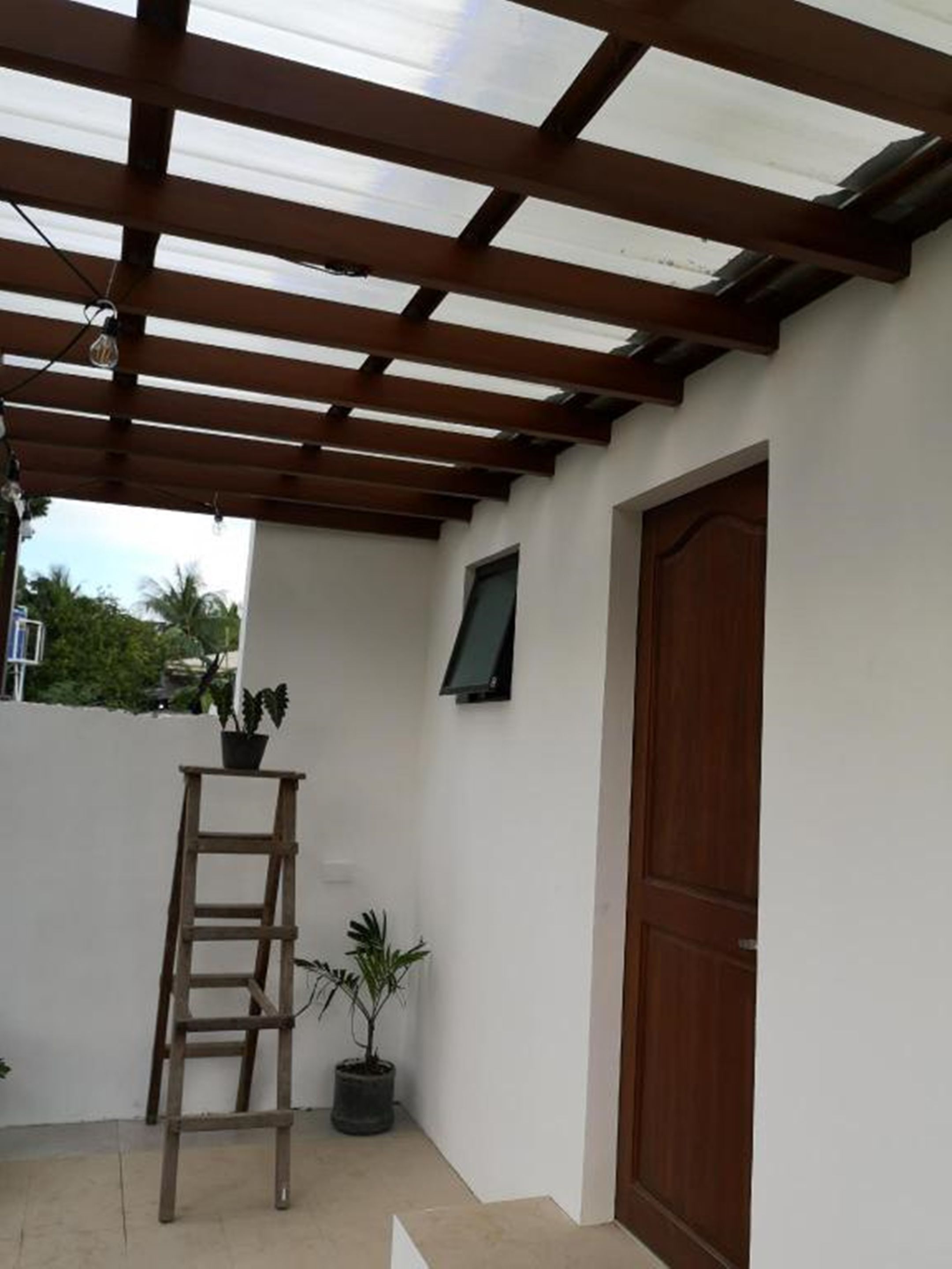 A covered patio area with a wooden ceiling, a wooden door, and a small table with plants.