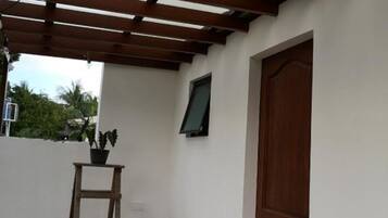 A covered patio area with a wooden ceiling, a wooden door, and a small table with plants.