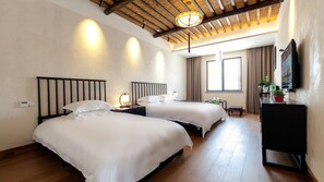 A hotel room with two beds, wooden flooring, a ceiling with exposed beams, a large window, and a flat-screen TV mounted on the wall.