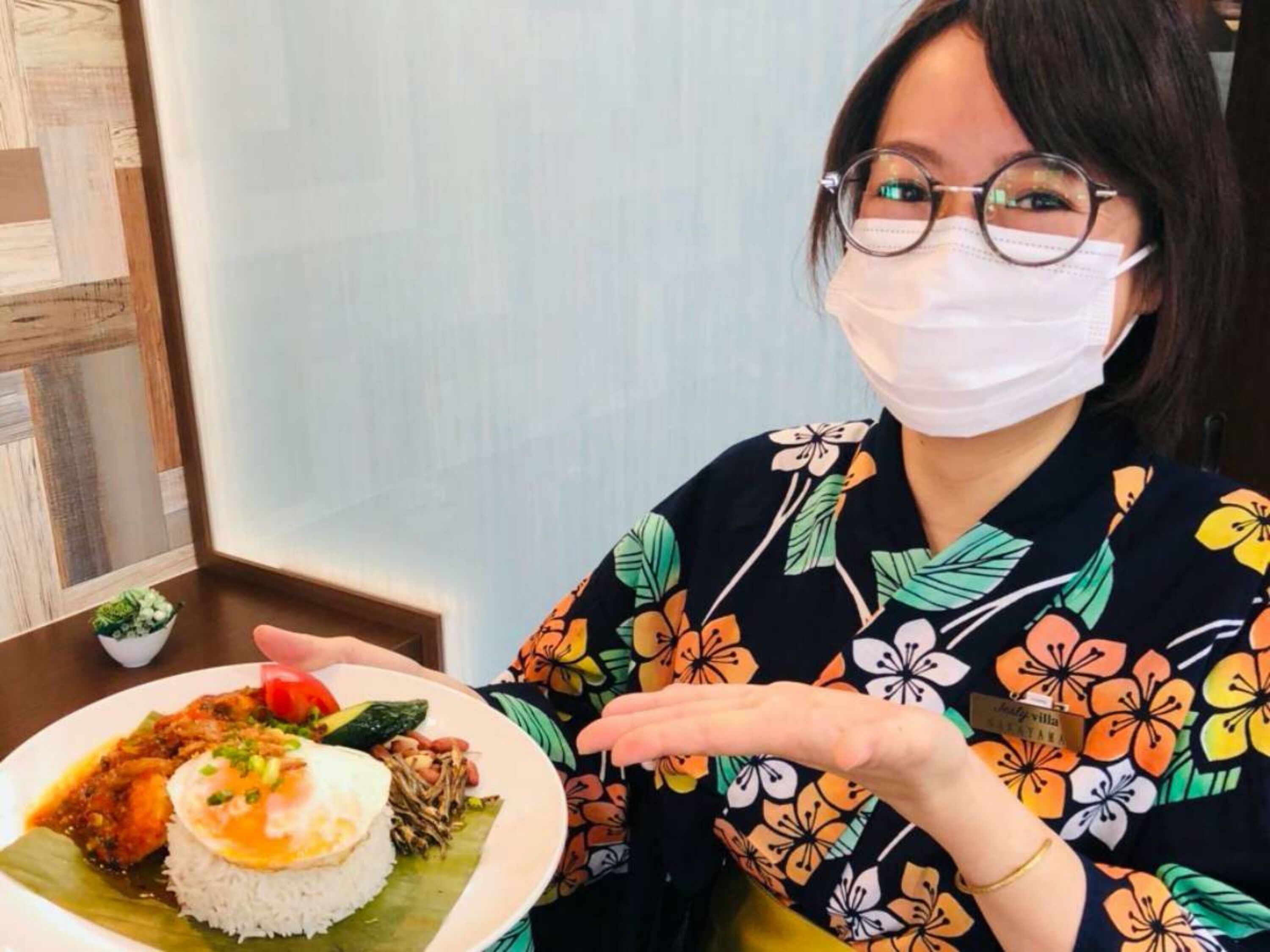 Una persona con kimono sosteniendo un plato de comida que incluye arroz, verduras y un huevo frito.