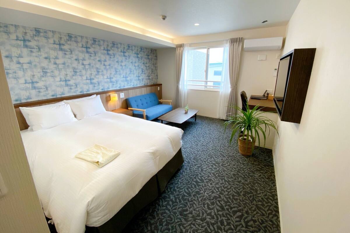 A hotel room with a large bed, a blue sofa, a small table, and a potted plant.