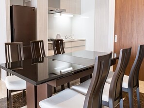 Een moderne eethoek met een tafel met glazen blad, zes stoelen en een inbouwkoelkast.