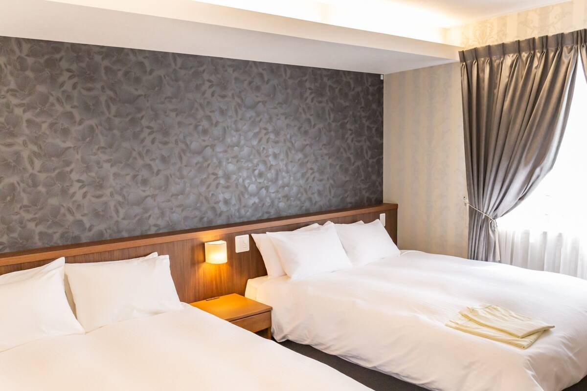 A hotel room with two beds, a stone-patterned headboard, a nightstand with a lamp, and a window with curtains.