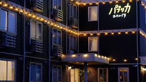 A building with multiple windows, some with curtains, and a neon sign in the upper right corner. - Paprika Hotel desu (Kisarazu)
