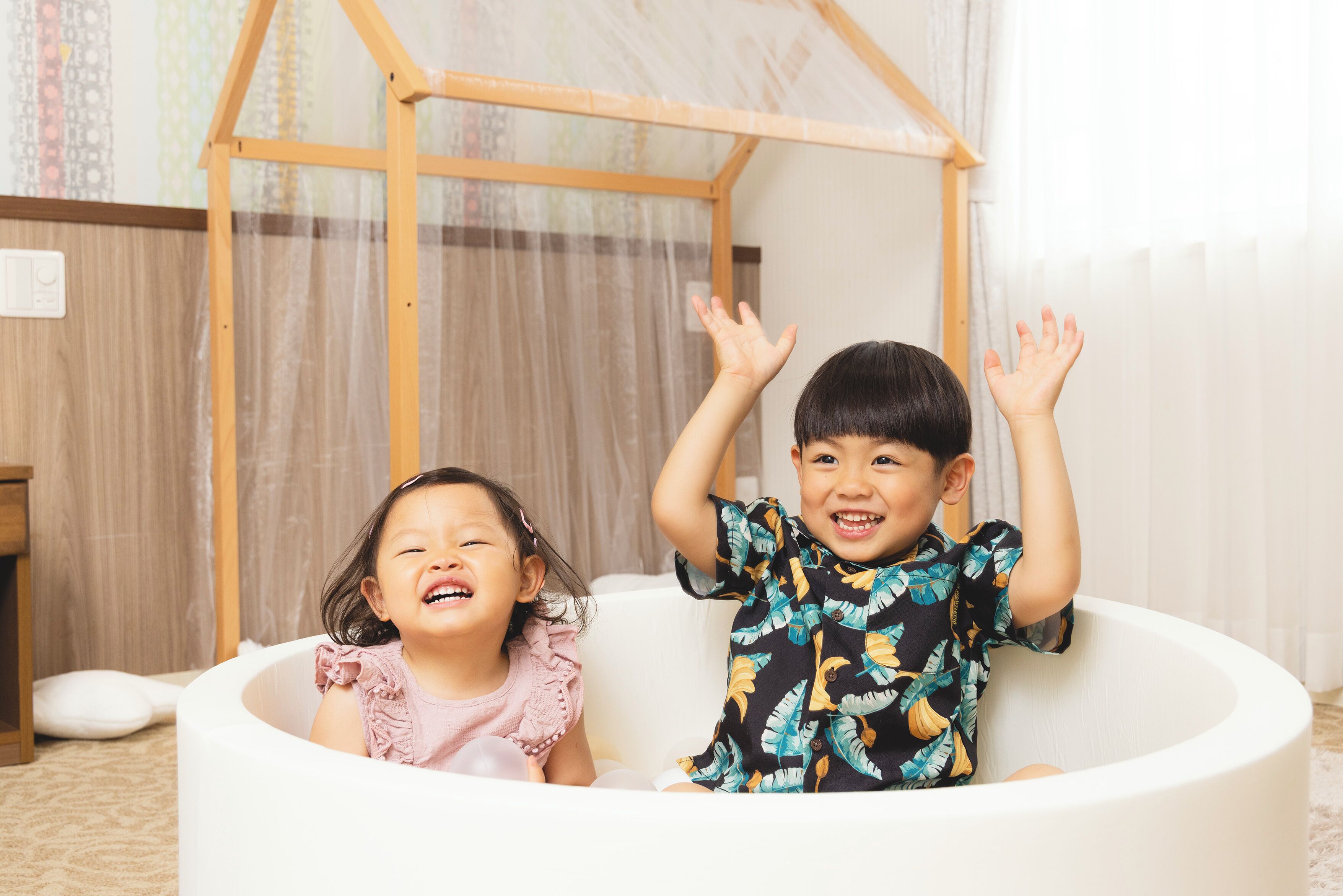 Dos niños en una bañera, con una casita de juegos de madera al fondo.