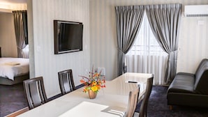 A hotel room with a dining table, chairs, a TV mounted on the wall, a sofa, and a bed. - Paprika Hotel desu (Kisarazu)