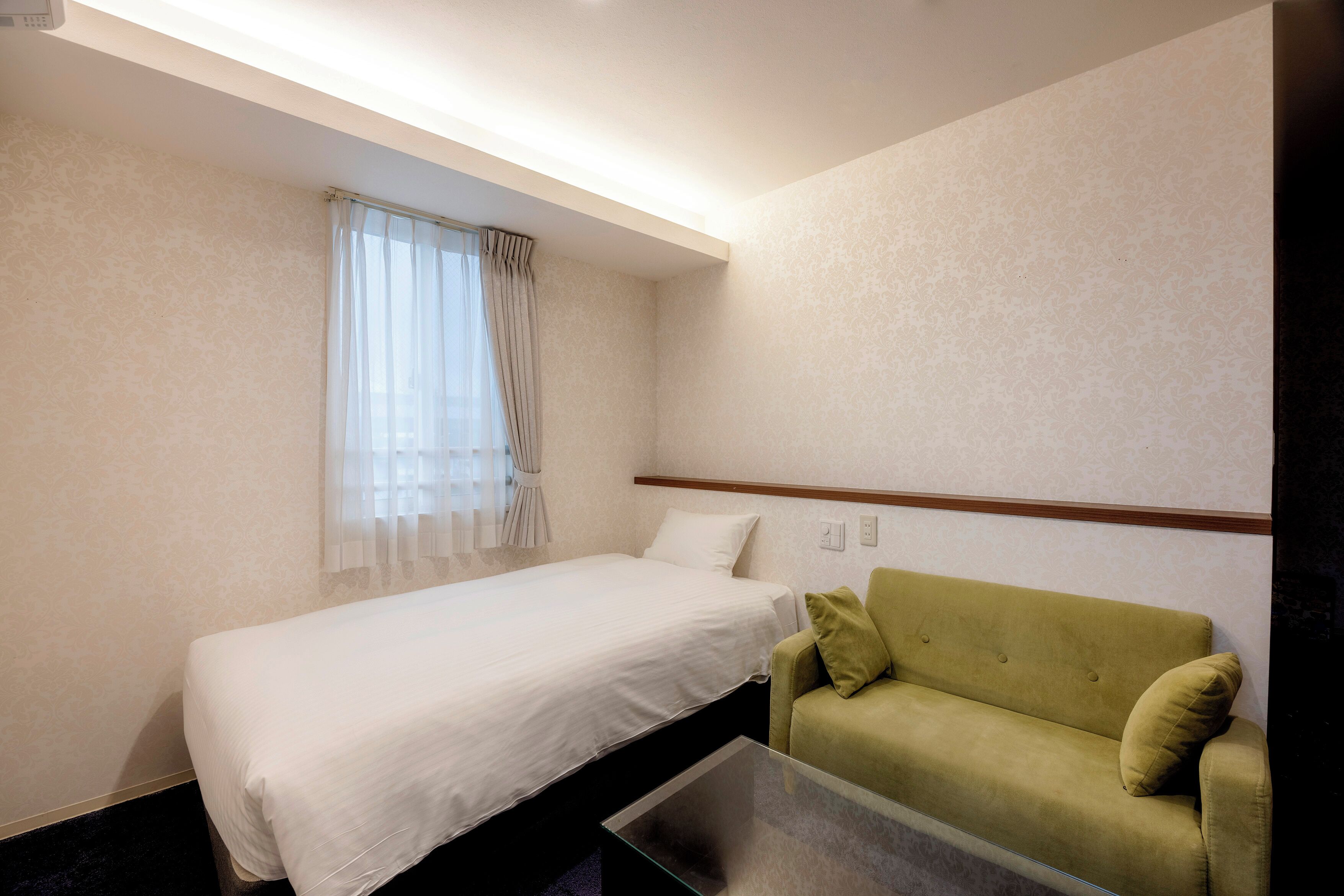 A hotel room with a bed, a green sofa, and a glass coffee table.