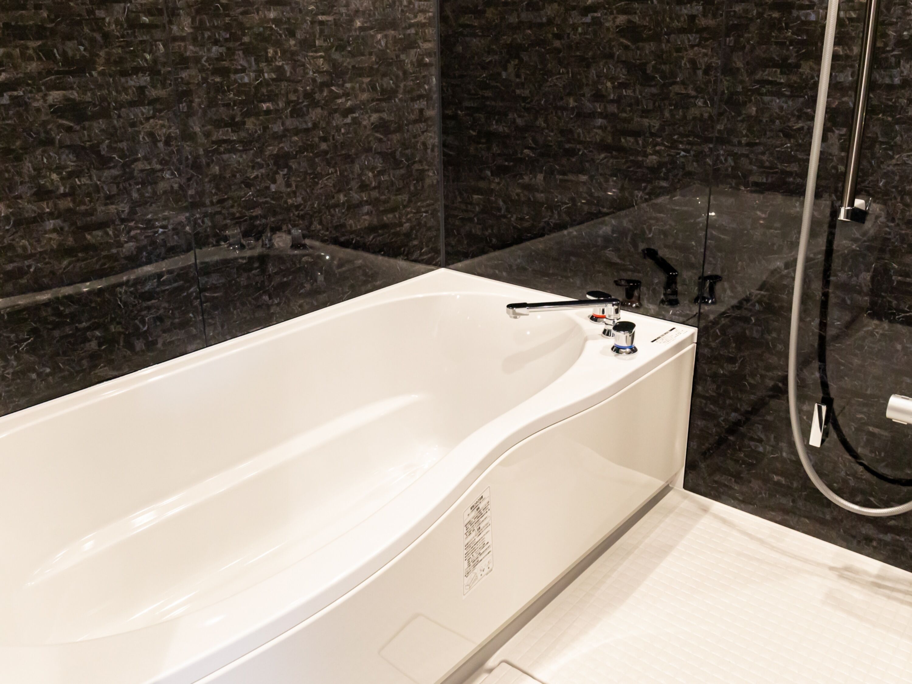 Ein modernes Badezimmer mit einer weißen Badewanne, dunklen Marmorwänden und einer Glasdusche.