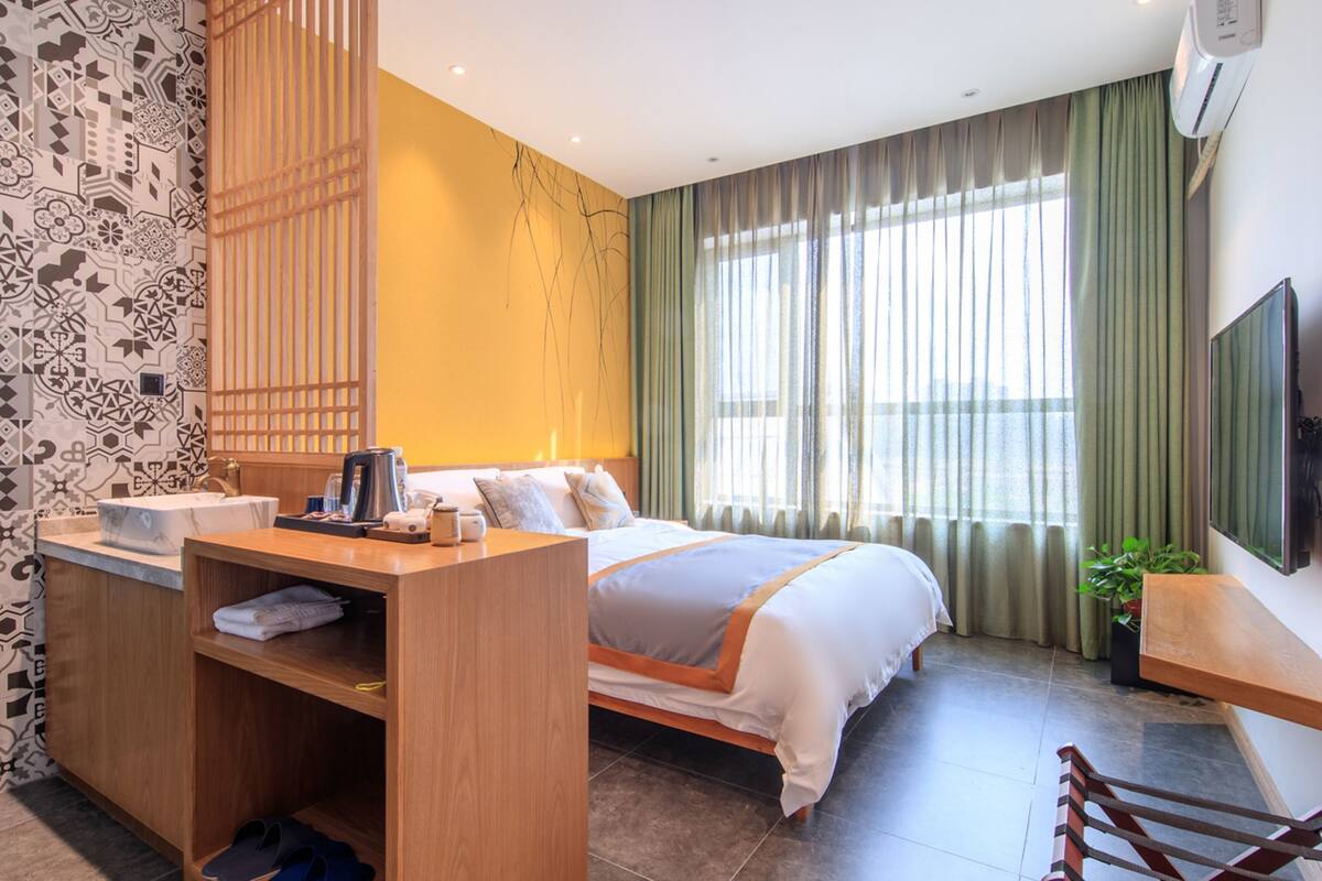 A hotel room with a bed, a desk with a chair, a TV, and a window with curtains.