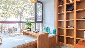 Une pièce avec un bureau et un banc en bois, une bibliothèque et une vue sur l’extérieur.