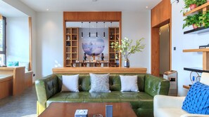 Un salon moderne avec un canapé en cuir vert, des étagères en bois et une grande œuvre d’art accrochée au mur.