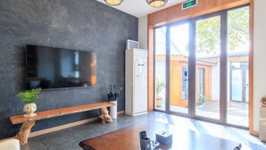 Un hall d’entrée moderne doté d’un téléviseur à écran plat, d’un banc en bois, d’une table basse et d’une grande porte vitrée donnant sur l’extérieur.