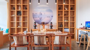 Un espace repas agrémenté d’une grande fresque murale ovale, de meubles en bois et d’étagères où sont exposés des objets décoratifs.