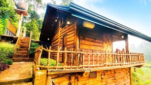 A rustic wooden cabin with a balcony, surrounded by lush greenery.