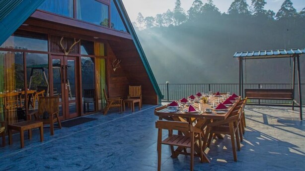A modern building with large glass windows, a dining area with wooden tables and chairs, and a view of the forested mountains in the background.