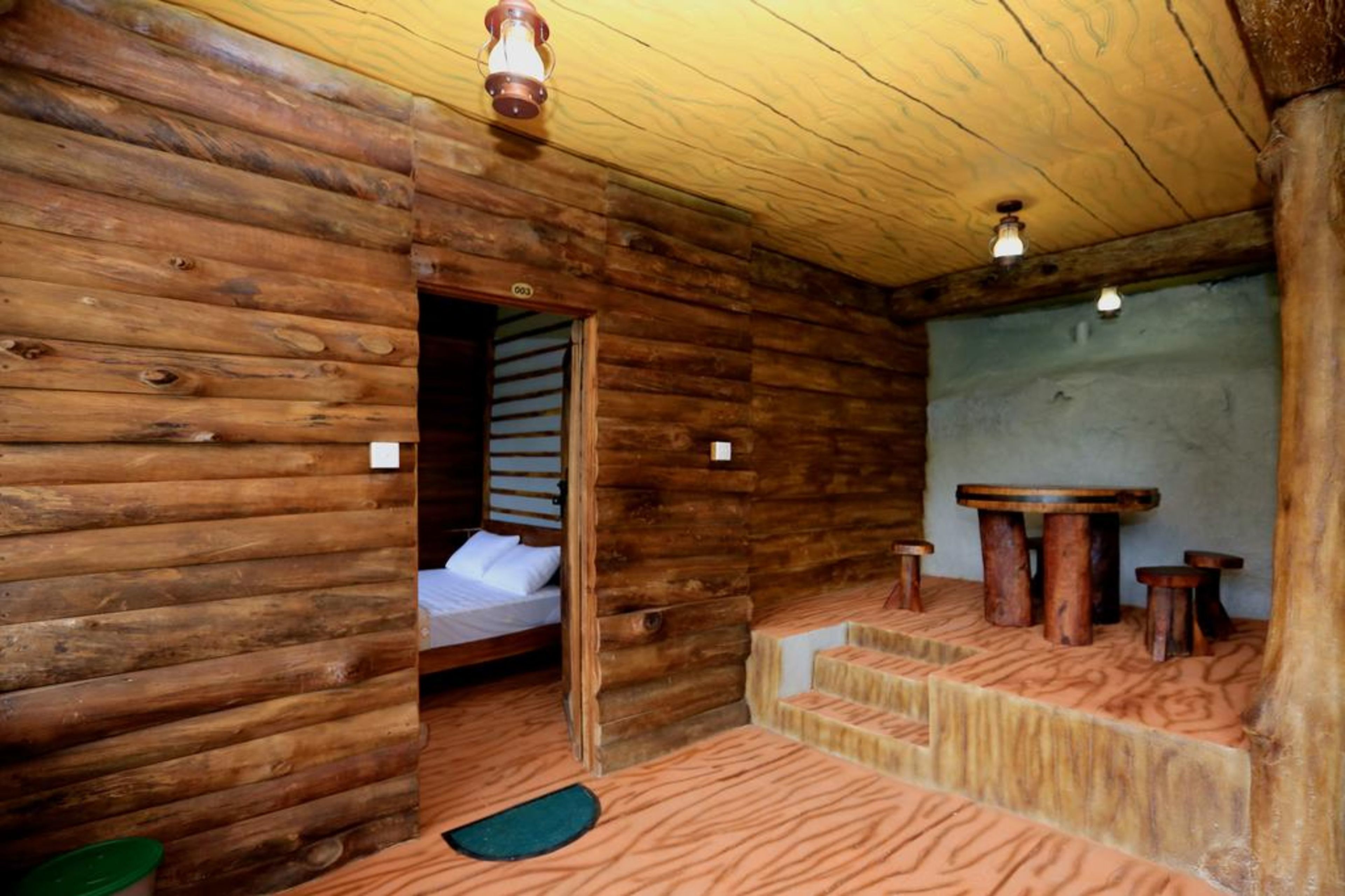 A log cabin room with a bed, a small table, and a bench.