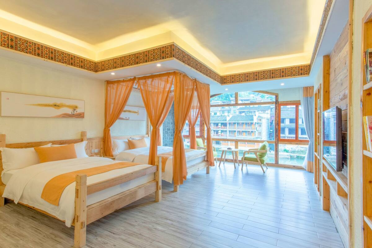 Ein Zimmer mit zwei Holzbetten, einem großen Fenster mit Blick auf traditionelle Gebäude und einem Bücherregal mit Büchern.