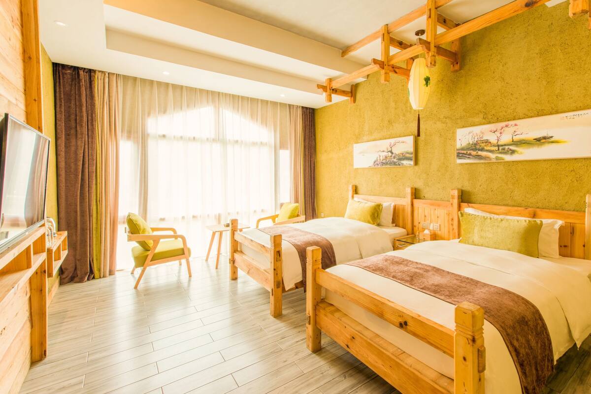 Ein Hotelzimmer mit Holzmöbeln, einem großen Bett, einem kleineren Bett, einem Fernseher und einem Fenster mit Vorhängen.
