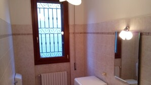 Casa de banho pequena com sanita, máquina de lavar roupa, lavatório e janela com grades.