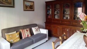 Uma sala de estar com um sofá cinzento, um armário de madeira e uma mesa de jantar com cadeiras.