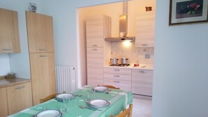 Uma área de refeições com mesa posta para quatro pessoas, armários de madeira, cozinha com fogão e uma moldura na parede.