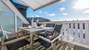 En balkon med et bord, stole og udsigt til himlen og det fjerne landskab.