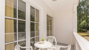 A balcony with a white table and chairs, large windows, and a view of greenery. - App. 1 (ground floor) - House Elise (Binz)