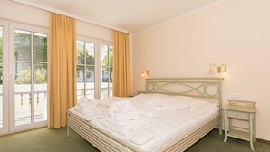 A neatly made bed with a folded towel, a bedside table with a lamp, and a window with curtains. - App. 1 (ground floor) - House Elise (Binz)