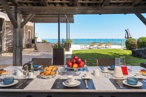 Uma área de refeições ao ar livre com uma mesa posta para café da manhã, com vista para uma piscina e o oceano.