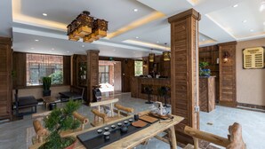 A modern lobby with wooden accents, a reception desk, seating areas, and a tea service setup. - Floral Hotel Xijiang Banshan Yunfu (Qiandongnan)