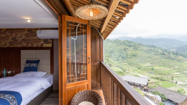 A bedroom with a bed, a wooden door, and a view of terraced fields. - Floral Hotel Xijiang Banshan Yunfu (Qiandongnan)