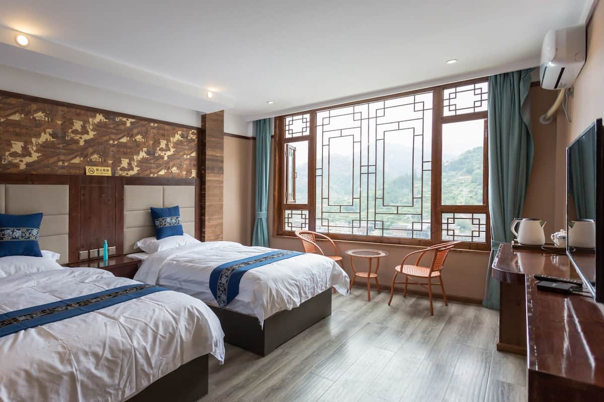 Une chambre d’hôtel avec deux lits, une petite table, une chaise, un téléviseur et une fenêtre donnant sur un beau paysage.