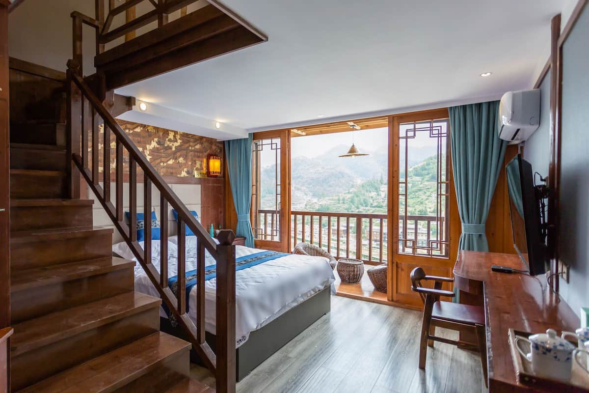Une chambre avec un escalier en bois, un lit, un bureau et une vue sur les montagnes.