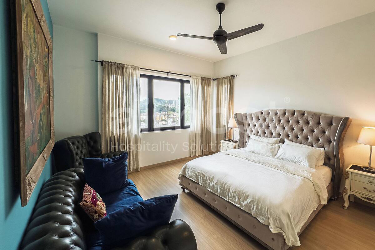 Une chambre dotée d’un grand lit, d’un coin salon avec un canapé, d’un ventilateur de plafond et d’une fenêtre avec des rideaux.