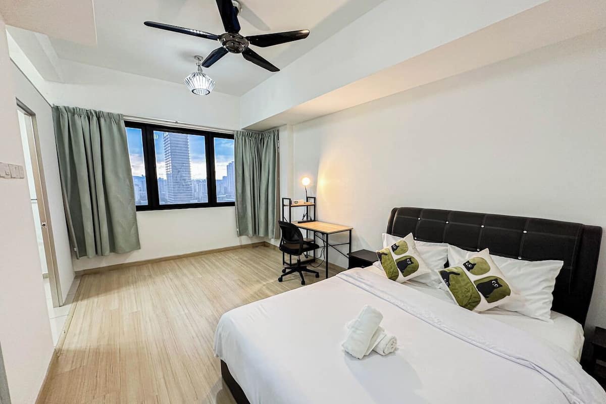 Une chambre d’hôtel équipée d’un lit, d’un bureau, d’une chaise et offrant une vue sur la ville grâce à de grandes fenêtres.