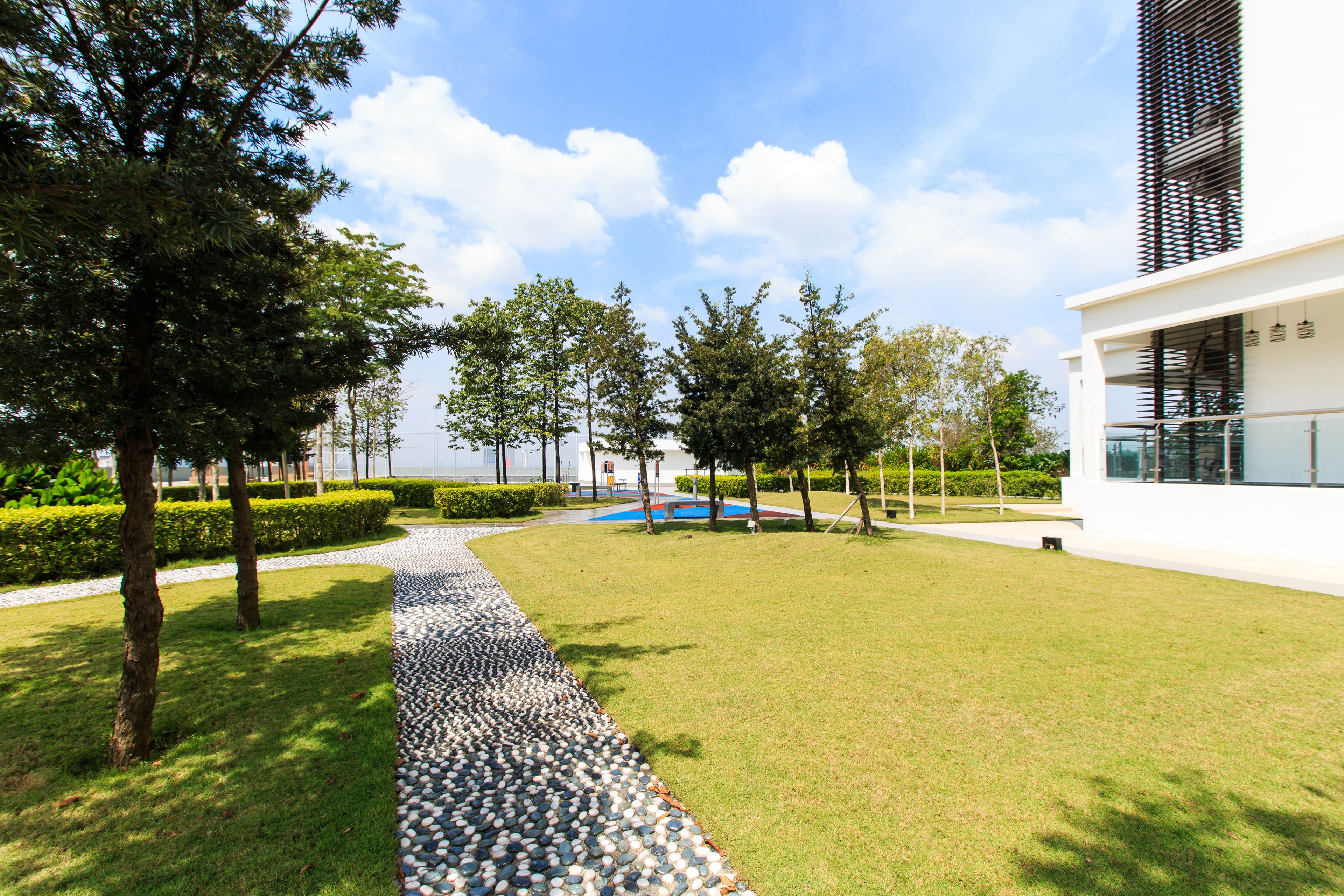 A modern building with a paved walkway, green lawns, and trees.