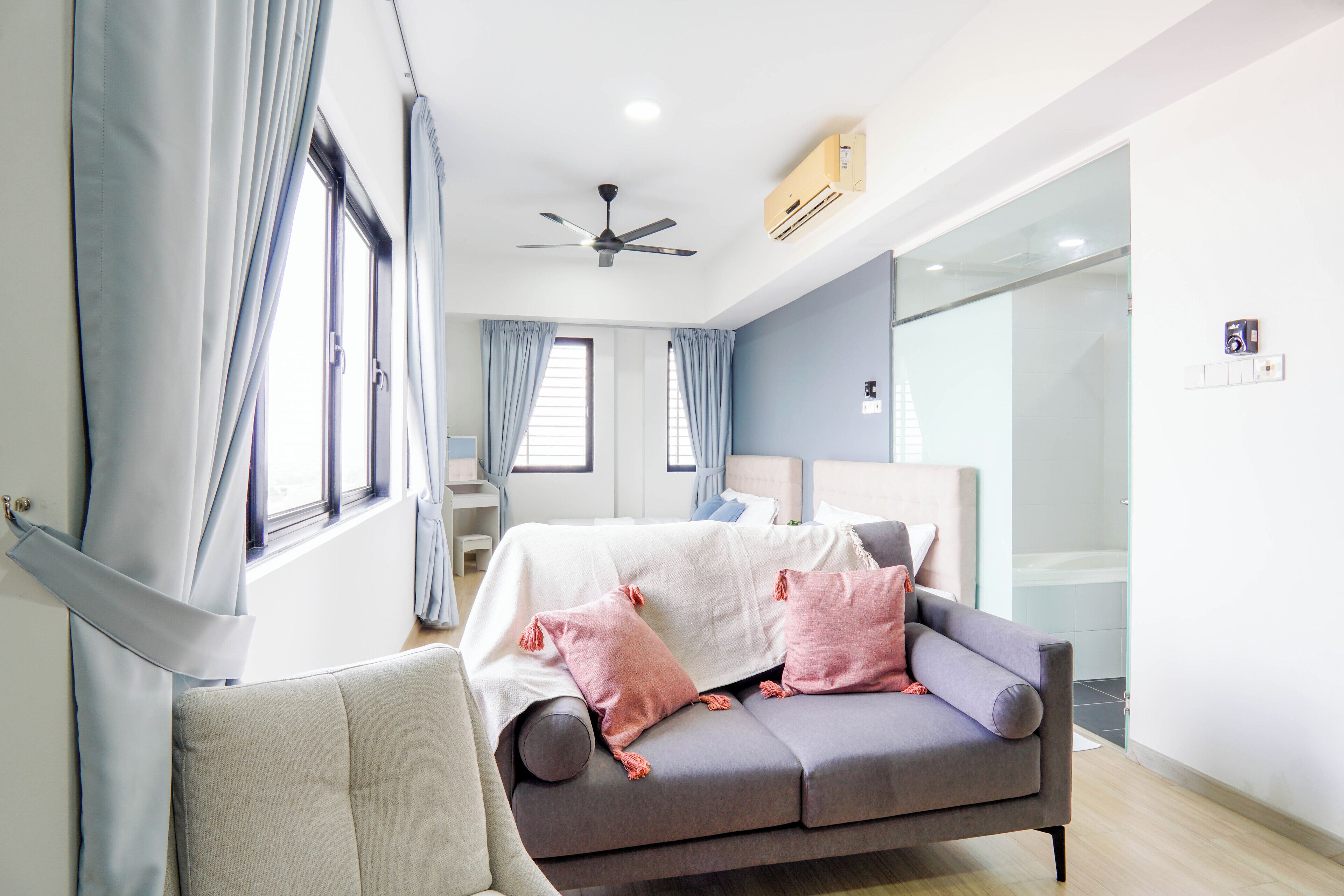 Een moderne slaapkamer met een grijze bank, een bed met een wit en roze deken, en een plafondventilator.