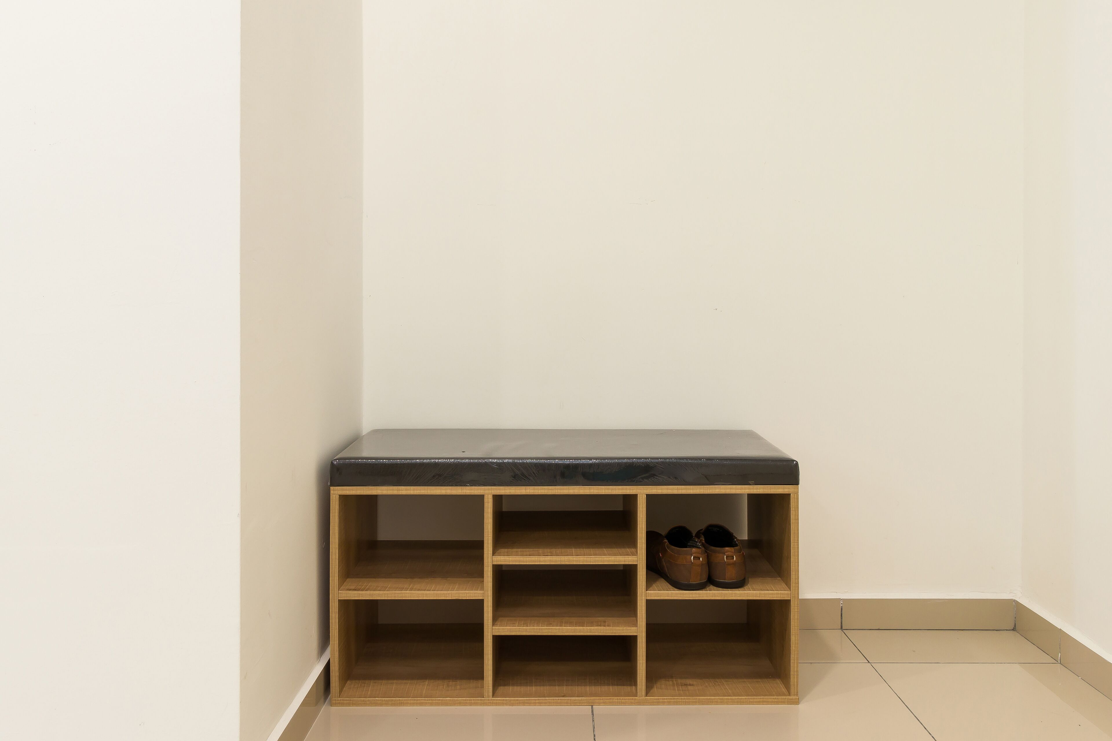 A corner with a wooden shoe rack against a wall, containing a pair of shoes.