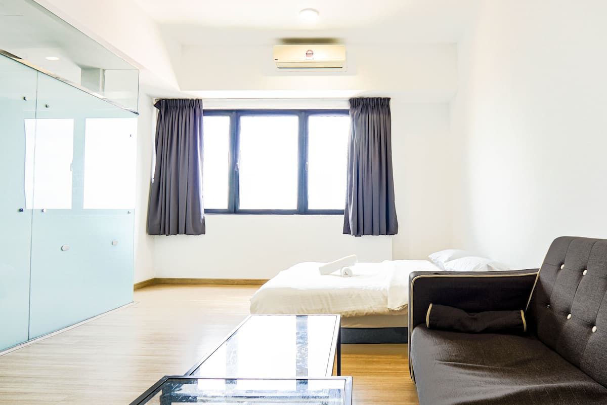Une chambre d’hôtel avec un lit, un canapé sombre, une table basse en verre et une armoire.
