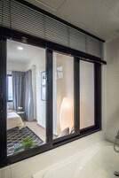 Un baño moderno con un ventanal amplio, una bañera y una mesita de noche con una planta.
