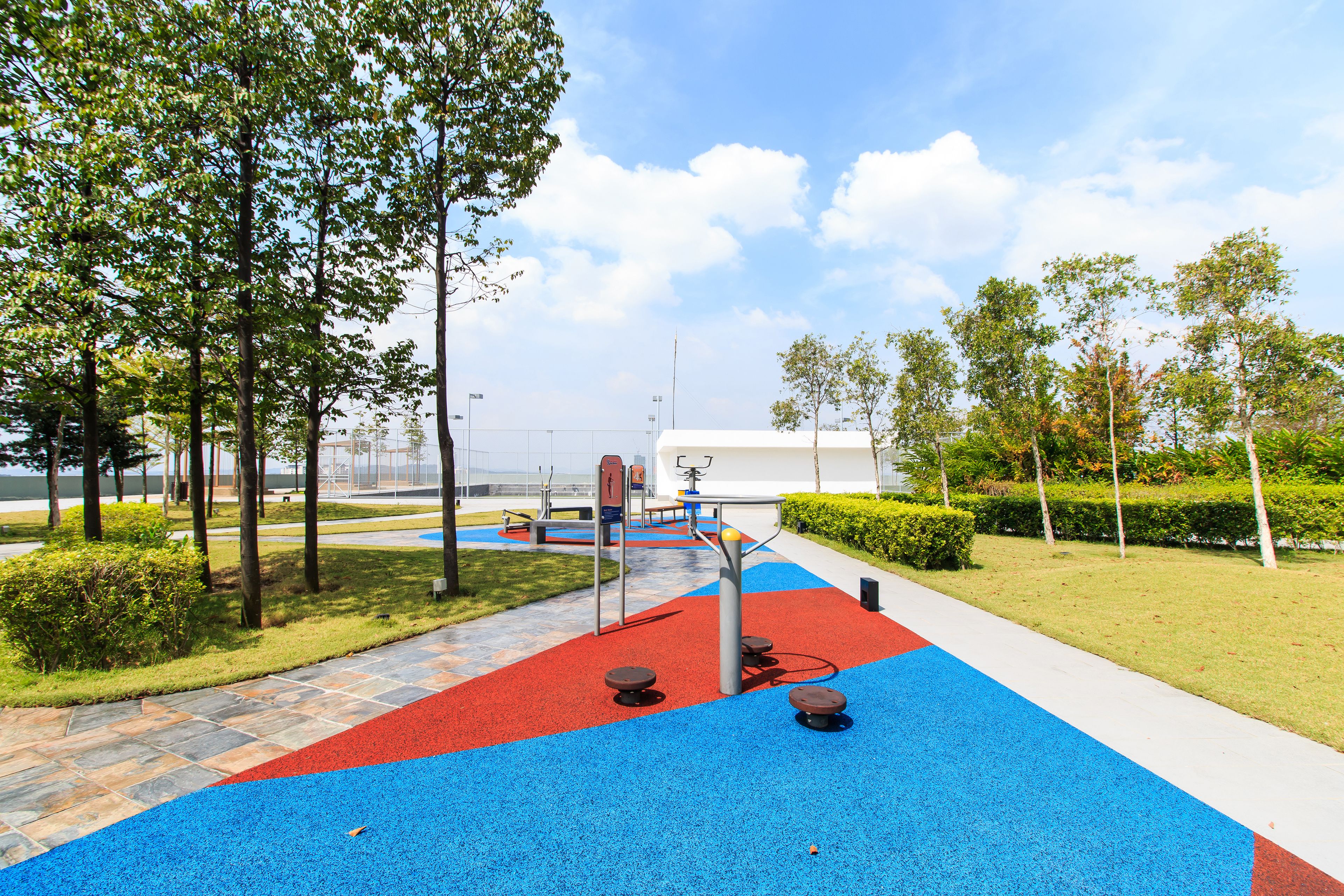 A playground with red and blue rubber flooring, exercise equipment, and trees.