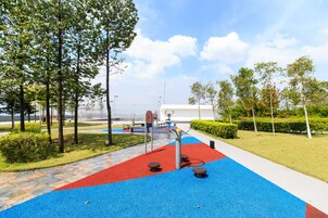 A playground with red and blue rubber flooring, exercise equipment, and trees.