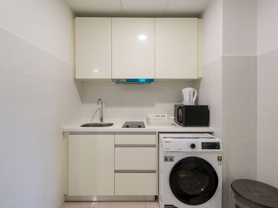Una cocina compacta con armarios blancos, un lavamanos, un microondas y una lavadora de carga frontal.