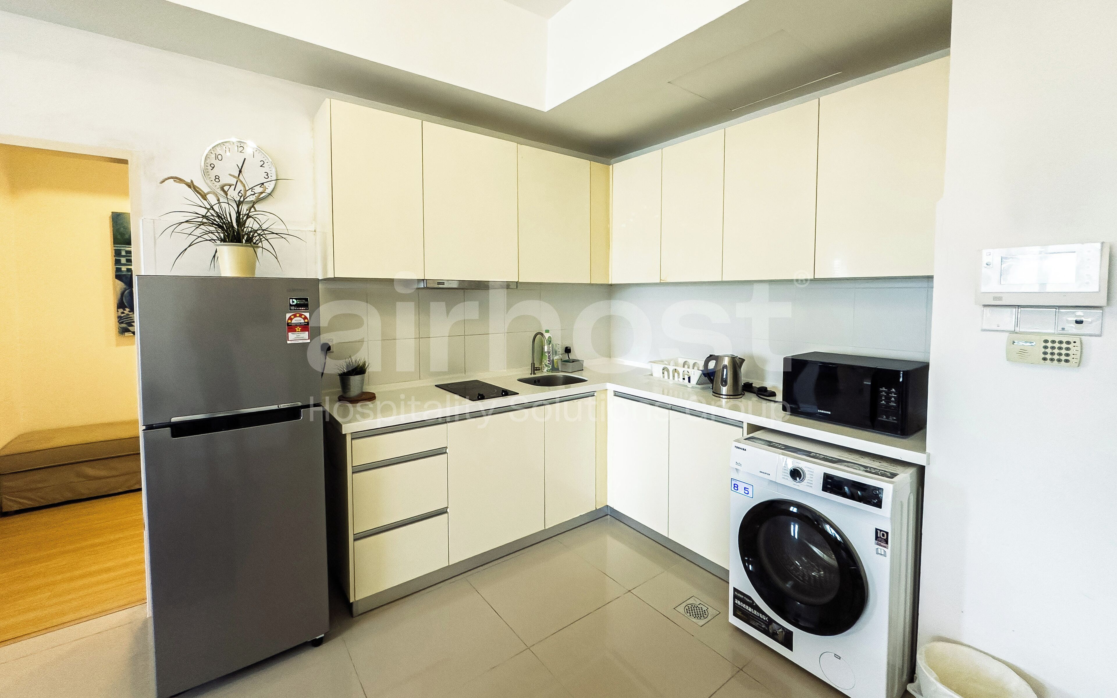 A modern kitchen with white cabinets, a stainless steel refrigerator, a built-in microwave, and a washing machine.