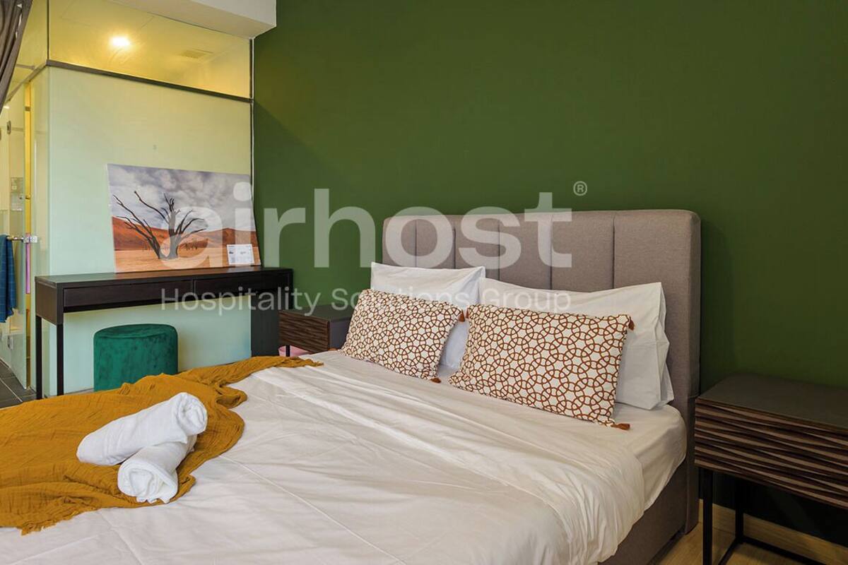 Une chambre d’hôtel avec un lit, un mur vert, un tableau et une fenêtre avec des rideaux.