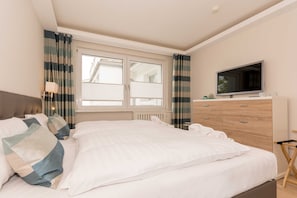 Een slaapkamer met een bed, een televisie, een dressoir en gordijnen.