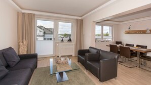 Un salon moderne avec une table basse en verre, un canapé, une table à manger avec des chaises et de grandes fenêtres avec des rideaux.