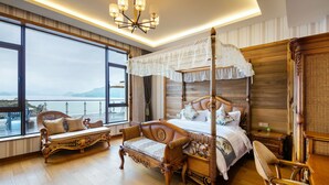 A spacious bedroom with a large window, a four-poster bed, a chaise lounge, and a wooden floor.
